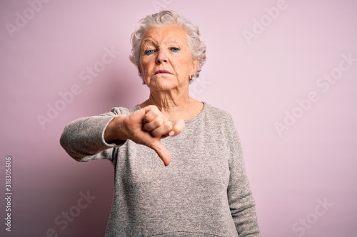 Senior beautiful woman wearing casual t-shirt standing over isolated pink background looking unhappy and angry showing rejection and negative with thumbs down gesture. Bad expression.