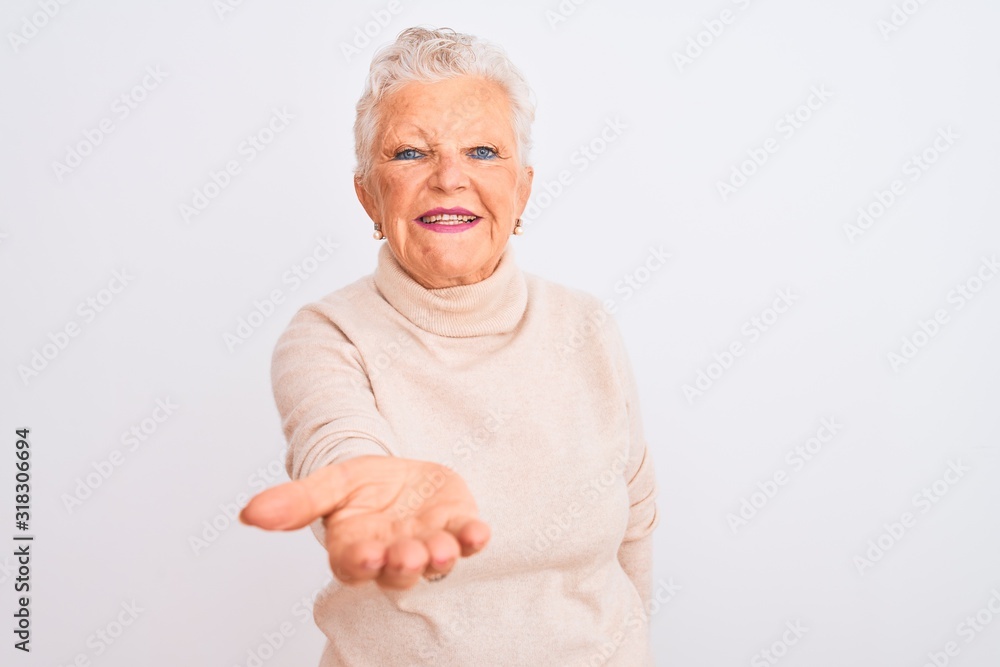 Senior grey-haired woman wearing turtleneck sweater standing over isolated white background smiling cheerful offering palm hand giving assistance and acceptance. Senior grey-haired woman wearing turtleneck sweater standing over isolated white background smiling cheerful offering palm hand giving assistance and acceptance.