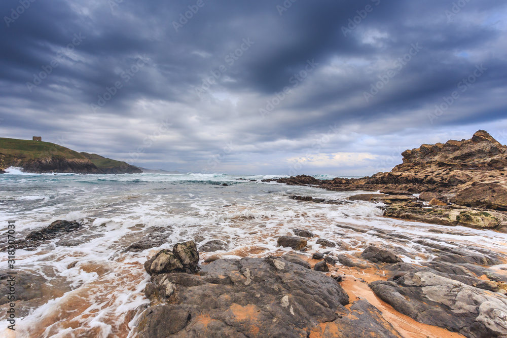 Tagle beach in winter with dramatic sky and waves against the rocks