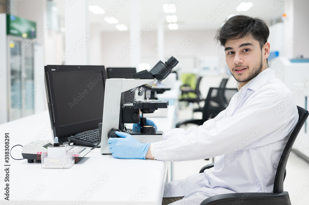 Portrait scientist man sitting and looking microscope in laboratory.Researcher using microscope in medical laboratory. Medical healthcare technology and pharmaceutical research concept.