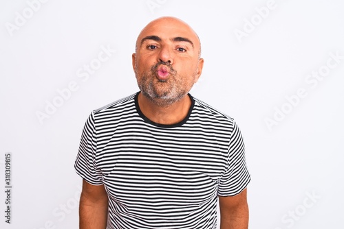 Middle age handsome man wearing striped navy t-shirt over isolated white background looking at the camera blowing a kiss on air being lovely and sexy. Love expression.