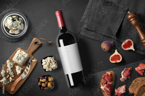 Cheese appetizer selection or wine snack set. Red wine, variety of cheese, figs, bread, olives and prosciutto on wooden board over black backdrop, top view, copy space