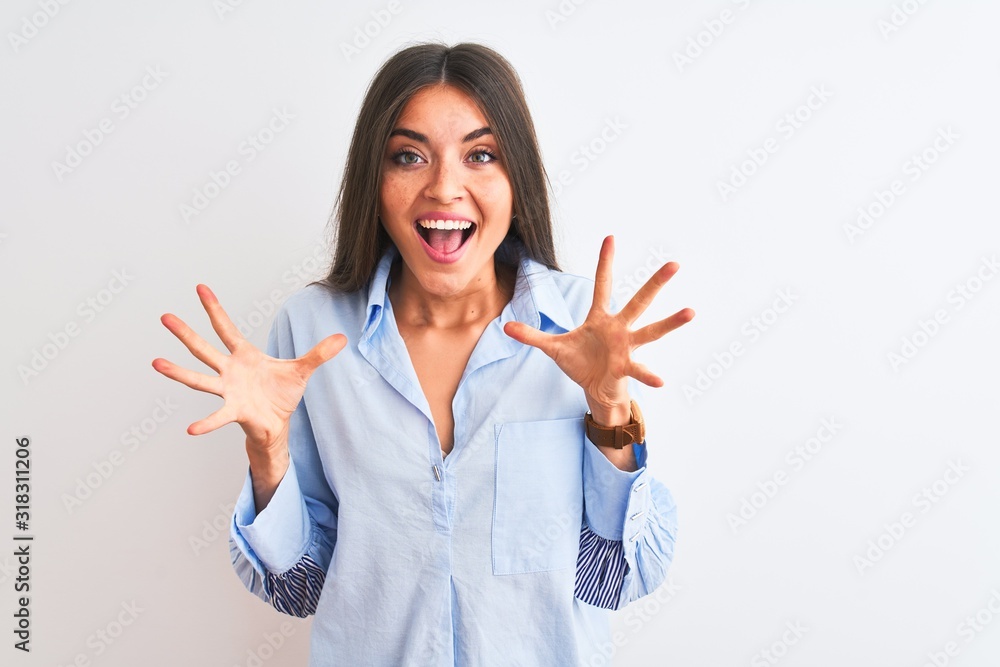 Young beautiful woman wearing blue elegant shirt standing over isolated white background celebrating crazy and amazed for success with arms raised and open eyes screaming excited. Winner concept Young beautiful woman wearing blue elegant shirt standing over isolated white background celebrating crazy and amazed for success with arms raised and open eyes screaming excited. Winner concept