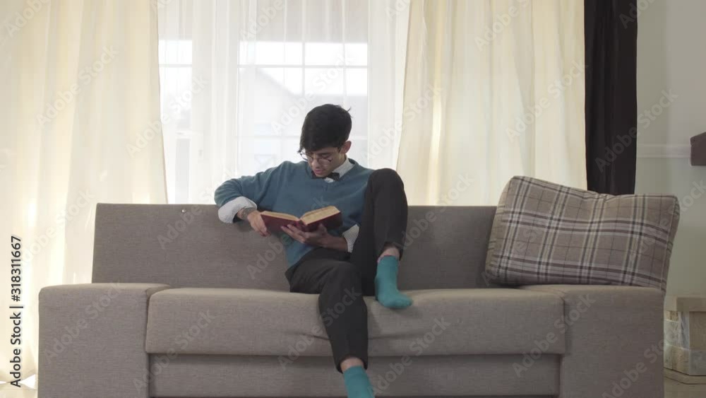 Portrait of focused Caucasian young man sitting on sofa and reading. Handsome university student resting on weekends with a book. Hobby, leisure, lifestyle. Portrait of focused Caucasian young man sitting on sofa and reading. Handsome university student resting on weekends with a book. Hobby, leisure, lifestyle.