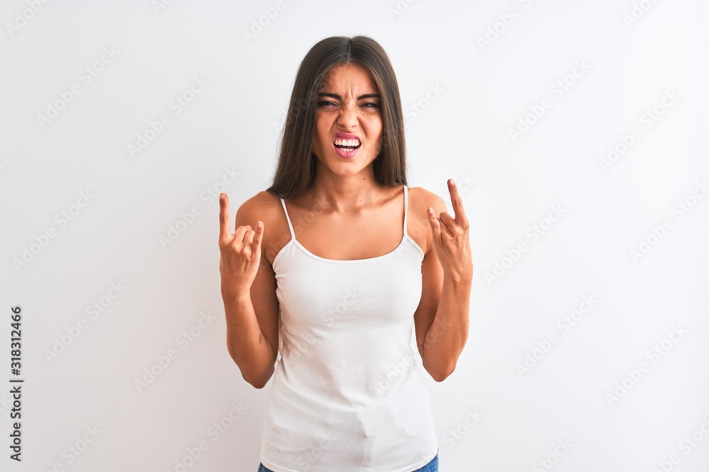 Young beautiful woman wearing casual t-shirt standing over isolated white background shouting with crazy expression doing rock symbol with hands up. Music star. Heavy concept. Young beautiful woman wearing casual t-shirt standing over isolated white background shouting with crazy expression doing rock symbol with hands up. Music star. Heavy concept.