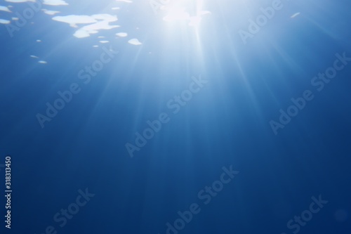 Sun beams shinning underwater . Trendy color classic blue background. © Tunatura