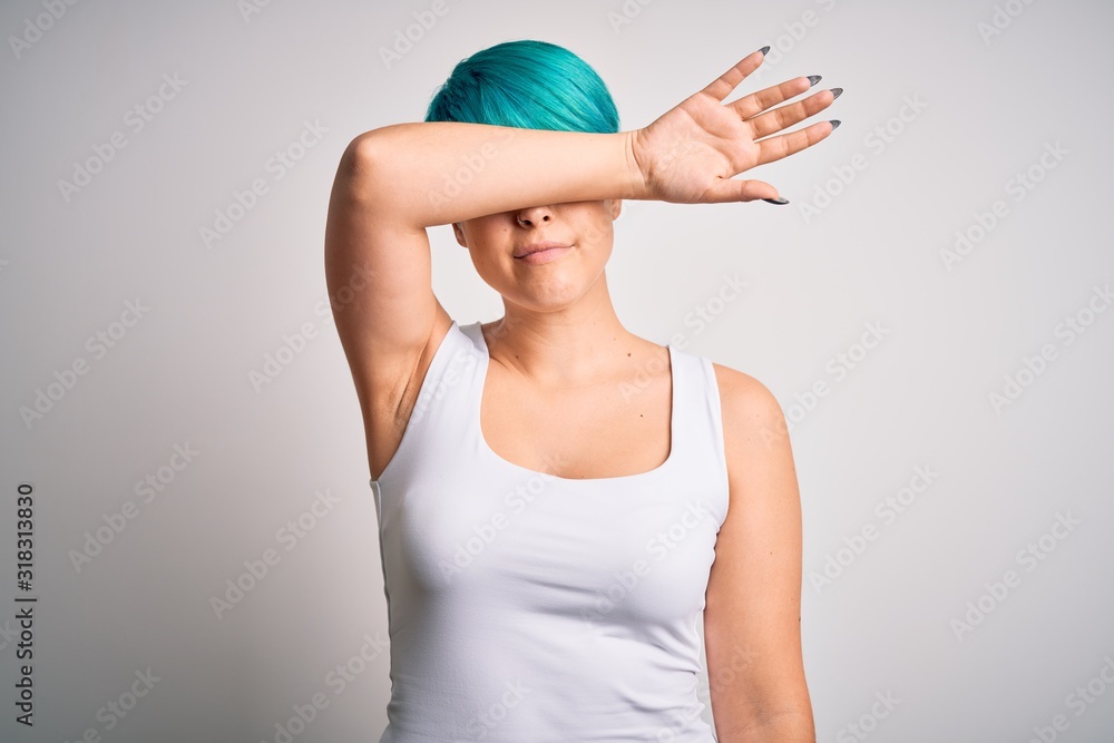 Young beautiful woman with blue fashion hair wearing casual t-shirt over white background covering eyes with arm, looking serious and sad. Sightless, hiding and rejection concept Young beautiful woman with blue fashion hair wearing casual t-shirt over white background covering eyes with arm, looking serious and sad. Sightless, hiding and rejection concept