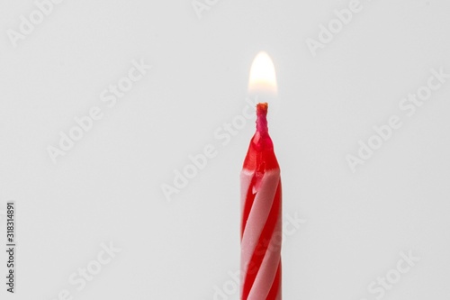 Red and white birthday candle lit on a white background. Birthday concept