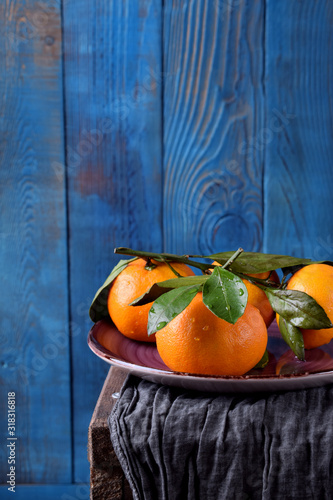 Mandarins with green leaves on the ceramic plate against the blue wooden background