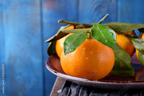 Mandarins with green leaves on the ceramic plate against the blue wooden background