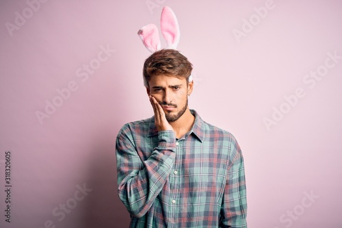 Young handsome adult man wearing cute easter rabbit ears over pink isolated background thinking looking tired and bored with depression problems with crossed arms. © Krakenimages.com