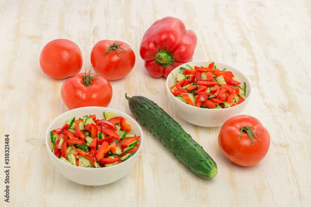 Vitamin salad of ripe, red tomatoes and fresh, green cucumbers in glass white bowl on light wooden table. Ingredients for salad. Vegetables. Concept of healthy eating Vitamin salad of ripe, red tomatoes and fresh, green cucumbers in glass white bowl on light wooden table. Ingredients for salad. Vegetables. Concept of healthy eating