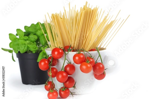 closeup of bowl with cherry tomatoes, spaghetti and basil jar on a white background