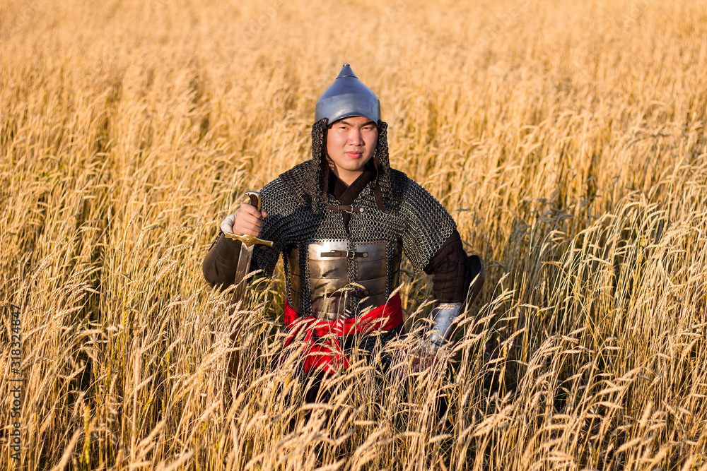 Asian warrior in oriental armor and with a saber in his hands sitting in a wheat field Asian warrior in oriental armor and with a saber in his hands sitting in a wheat field