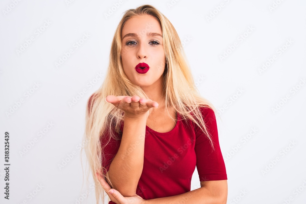 Young beautiful woman wearing red t-shirt standing over isolated white background looking at the camera blowing a kiss with hand on air being lovely and sexy. Love expression. Young beautiful woman wearing red t-shirt standing over isolated white background looking at the camera blowing a kiss with hand on air being lovely and sexy. Love expression.