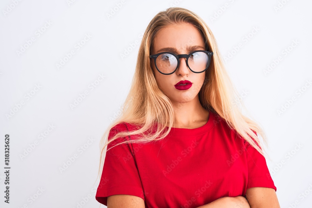 Young beautiful woman wearing red t-shirt and glasses standing over isolated white background skeptic and nervous, disapproving expression on face with crossed arms. Negative person. Young beautiful woman wearing red t-shirt and glasses standing over isolated white background skeptic and nervous, disapproving expression on face with crossed arms. Negative person.