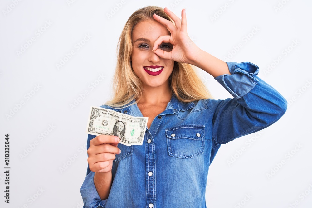Young beautiful blond woman holding dollar standing over isolated white background with happy face smiling doing ok sign with hand on eye looking through fingers Young beautiful blond woman holding dollar standing over isolated white background with happy face smiling doing ok sign with hand on eye looking through fingers