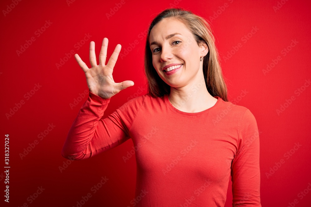 Young beautiful blonde woman wearing casual t-shirt standing over isolated red background showing and pointing up with fingers number five while smiling confident and happy. Young beautiful blonde woman wearing casual t-shirt standing over isolated red background showing and pointing up with fingers number five while smiling confident and happy.