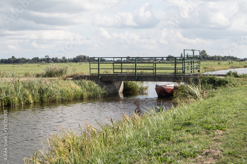 Mijdrecht / Netherlands - September 13, 2019 : Concrete bridge over irigation canal with small boat moored beneath with fields photo