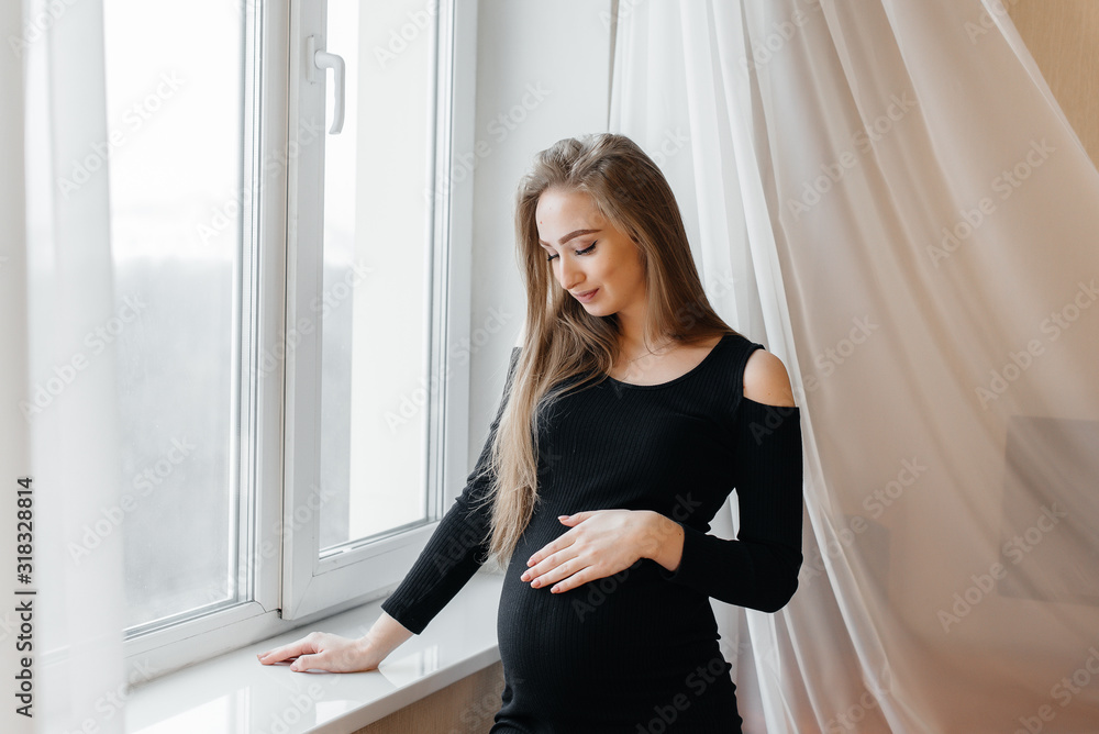 A beautiful pregnant girl is standing in a room near the window A beautiful pregnant girl is standing in a room near the window