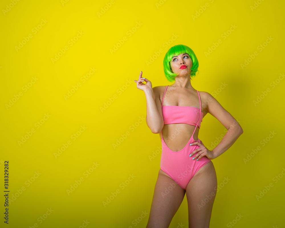 Beautiful woman in a green short wig and pink bikini posing on a yellow background. Portrait of a girl with sensual red lips. Beautiful woman in a green short wig and pink bikini posing on a yellow background. Portrait of a girl with sensual red lips.