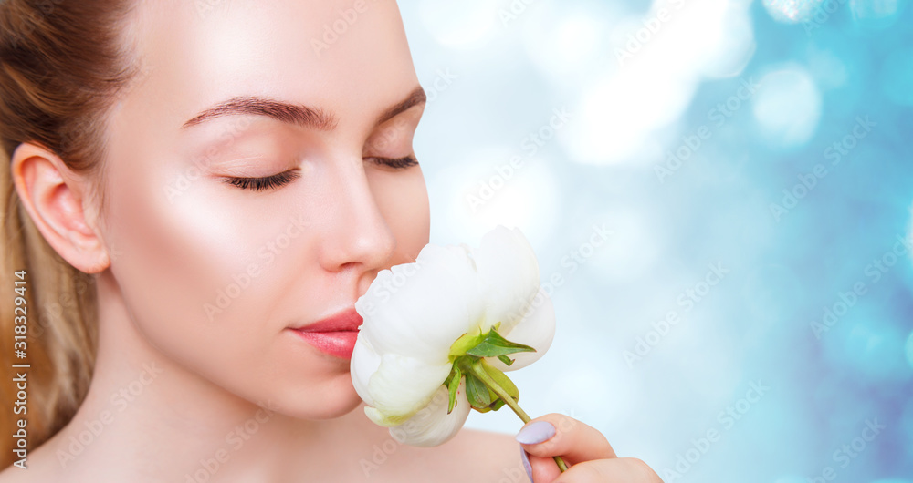 Young woman with perfect skin and white peony flower over blue bokeh background.