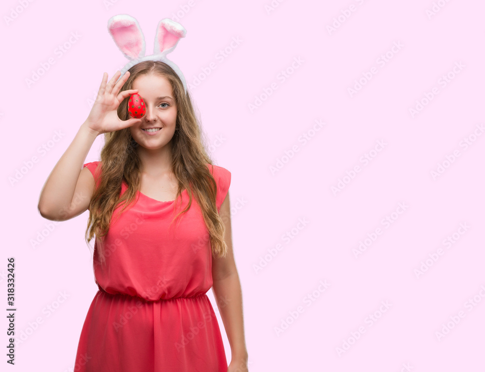 Young blonde woman wearing easter bunny ears with a happy face standing and smiling with a confident smile showing teeth
