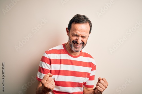 Middle age hoary man wearing casual striped t-shirt standing over isolated white background very happy and excited doing winner gesture with arms raised, smiling and screaming for success. Celebration