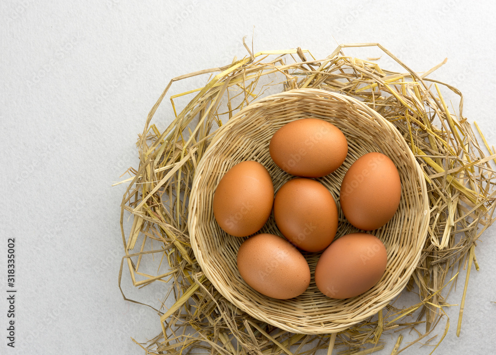 Brown chicken eggs in a basket on a separate straw on a white background.