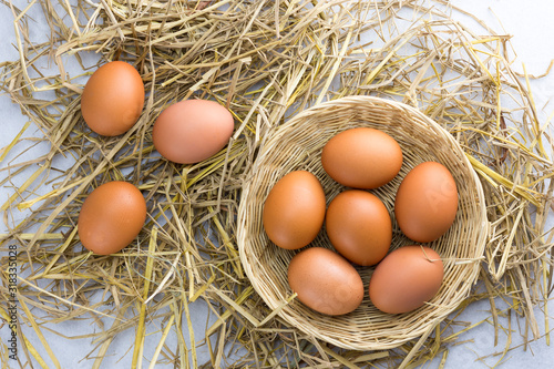 Brown chicken eggs in a basket on a separate straw on a white background.