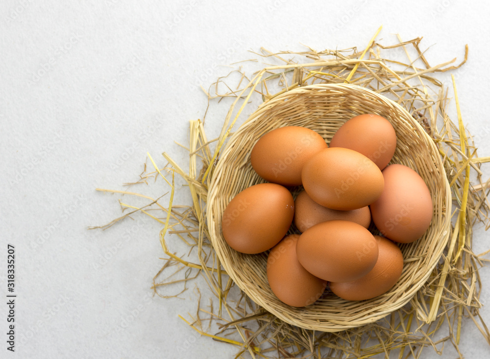 Brown chicken eggs in a basket on a separate straw on a white background.