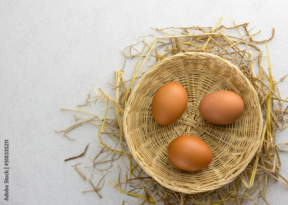 Brown chicken eggs in a basket on a separate straw on a white background.