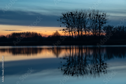 Trees on the shore of the lake, mirror image of evening clouds in the water in eastern Poland