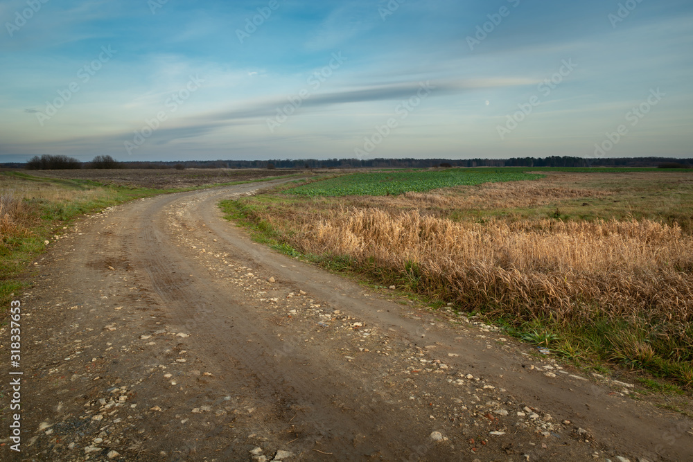 Dirt road with stones through the fields, dispelled clouds on the sky