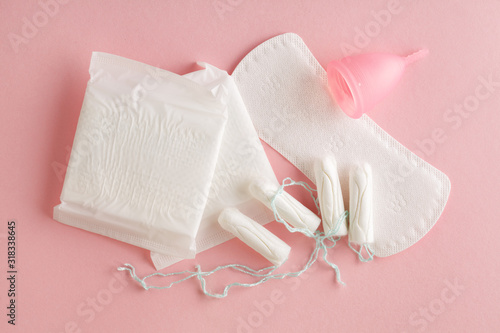 menstruation cycle, feminine hygiene and protection products, sanitary pads, tampons and menstrual cup on pastel pink background, top view, flat layout photo