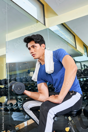 Low angle shot of confident young Asian man doing exercise with dumbbell in spa resort hotel gym