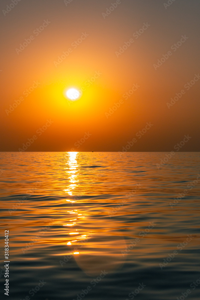 Bright sunset with large yellow sun under the sea surface. Beautiful sunset over the sea