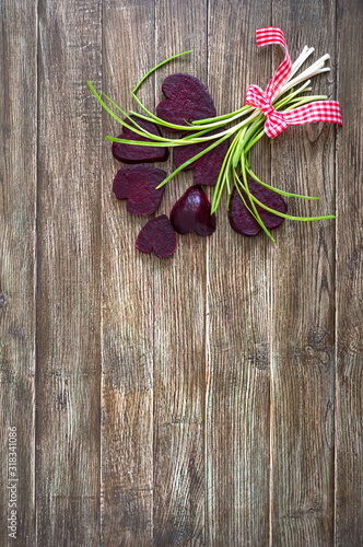 A bouquet of flowers from slices of boiled beets and green onions on a wooden background. To love beets. Healthy eating concept. Happy Valentine's Day. Copy space