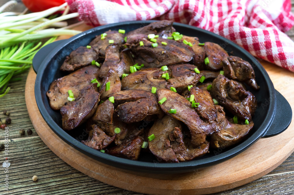 Fried chicken liver with young green onions in a cast-iron frying pan on a wooden background. Tasty healthy dish
