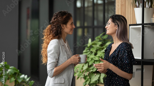 Tableau sur toile Multiethnic female colleagues chat during coffee break
