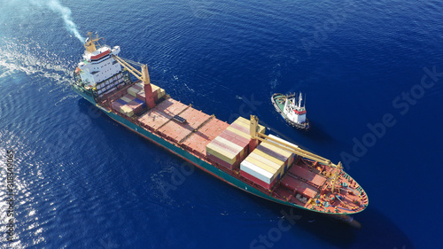 Aerial top down photo of Container cargo Ship carrying load in truck-size colourful containers in deep blue open ocean sea  © aerial-drone