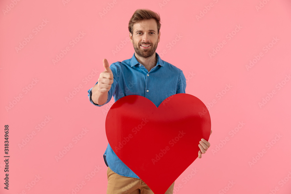 happy casual guy holding big heart and making thumbs up sign happy casual guy holding big heart and making thumbs up sign