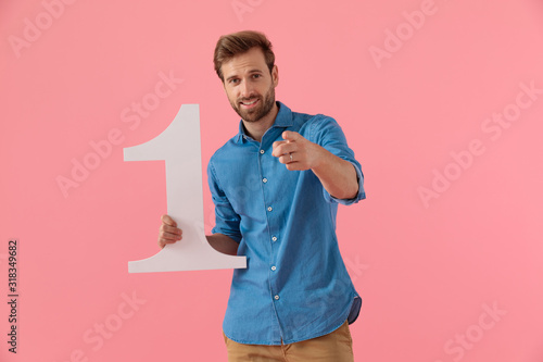 Foto happy casual guy holding number one sign and pointing finger