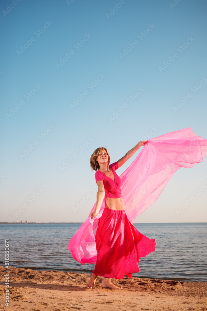 Girl in long dress on beach by sea. Woman with a long cloth near water. Model in a bright long skirt on vacation by  ocean.