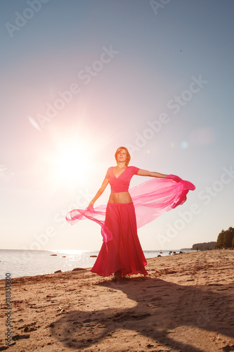 Girl in long dress on beach by sea. Woman with a long cloth near water. Model in a bright long skirt on vacation by ocean.
