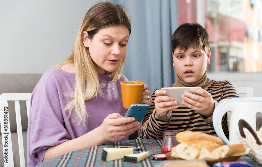 Portrait of young mother and son  using phones during breakfast