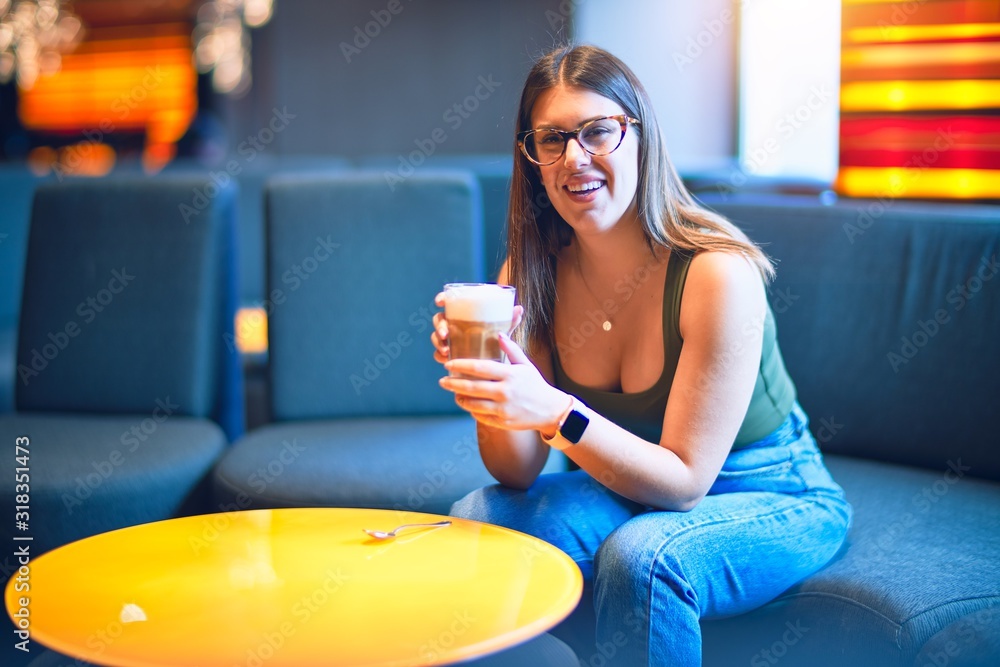Young beautiful woman smiling happy and confident. Sitting with smile on face holding glass of coffee at restaurant Young beautiful woman smiling happy and confident. Sitting with smile on face holding glass of coffee at restaurant