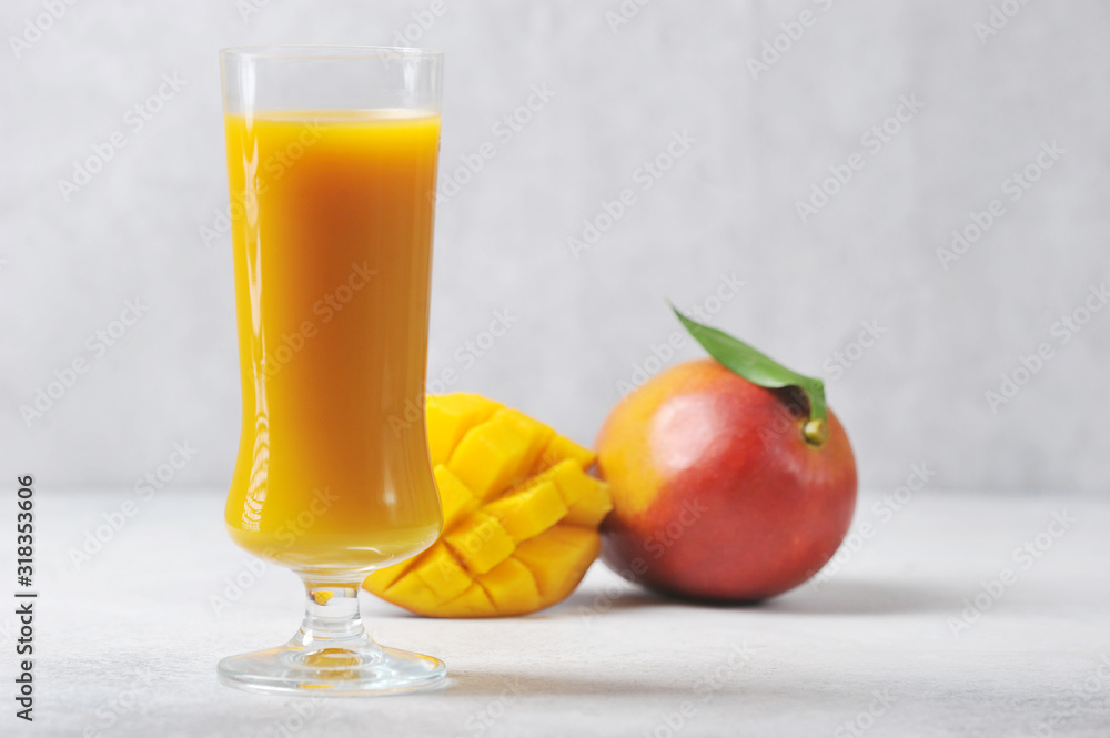 Mango juice in a tall glass. The whole Mango and half of the fruit complete the composition. Light background. Close-up. Mango juice in a tall glass. The whole Mango and half of the fruit complete the composition. Light background. Close-up.
