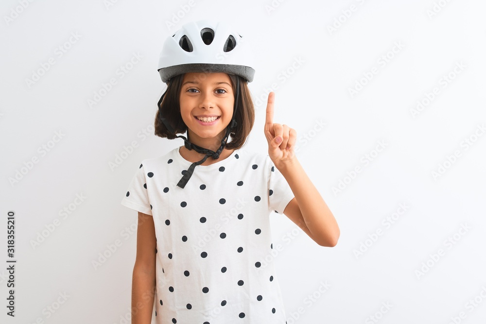 Beautiful child girl wearing security bike helmet standing over isolated white background showing and pointing up with finger number one while smiling confident and happy. Beautiful child girl wearing security bike helmet standing over isolated white background showing and pointing up with finger number one while smiling confident and happy.