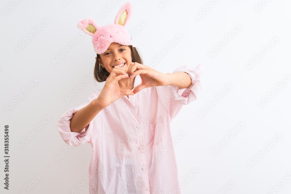 Beautiful child girl wearing sleep mask and pajama standing over isolated white background smiling in love doing heart symbol shape with hands. Romantic concept. Beautiful child girl wearing sleep mask and pajama standing over isolated white background smiling in love doing heart symbol shape with hands. Romantic concept.